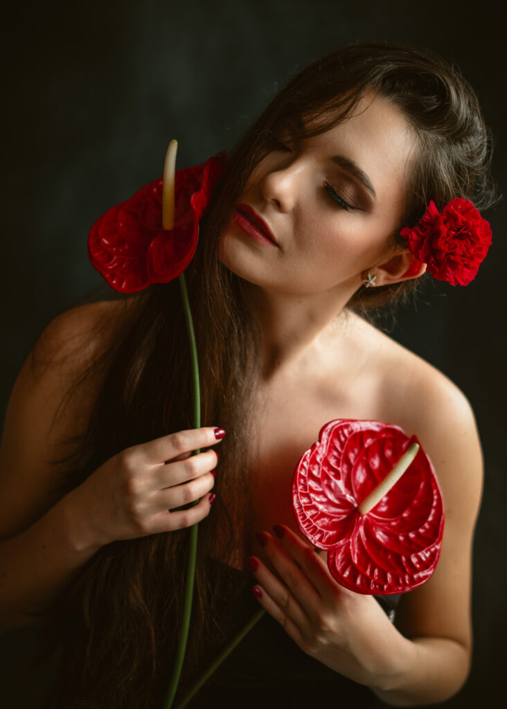 Kobieta z czerwonym kwiatem we włosach trzymająca dwa egzotyczne kwiaty anturium, artystyczna i zmysłowa fotografia portretowa w studyjnym świetle.