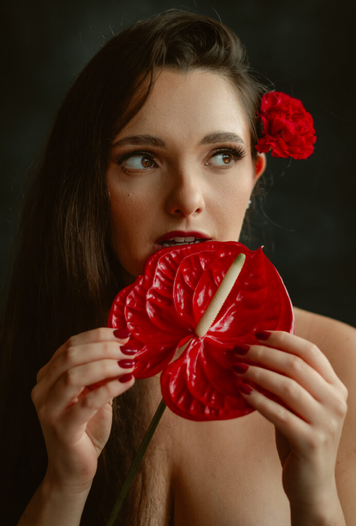 Kobieta z czerwonym kwiatem we włosach trzymająca w dłoniach egzotyczny kwiat anturium, zmysłowa fotografia portretowa w studyjnym świetle.