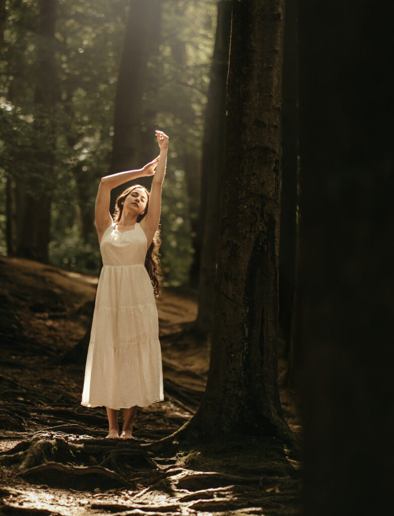 Kobieta w białej, zwiewnej sukience idąca boso przez las, fotografia portretowa w naturalnym świetle — profesjonalna sesja zdjęciowa w plenerze