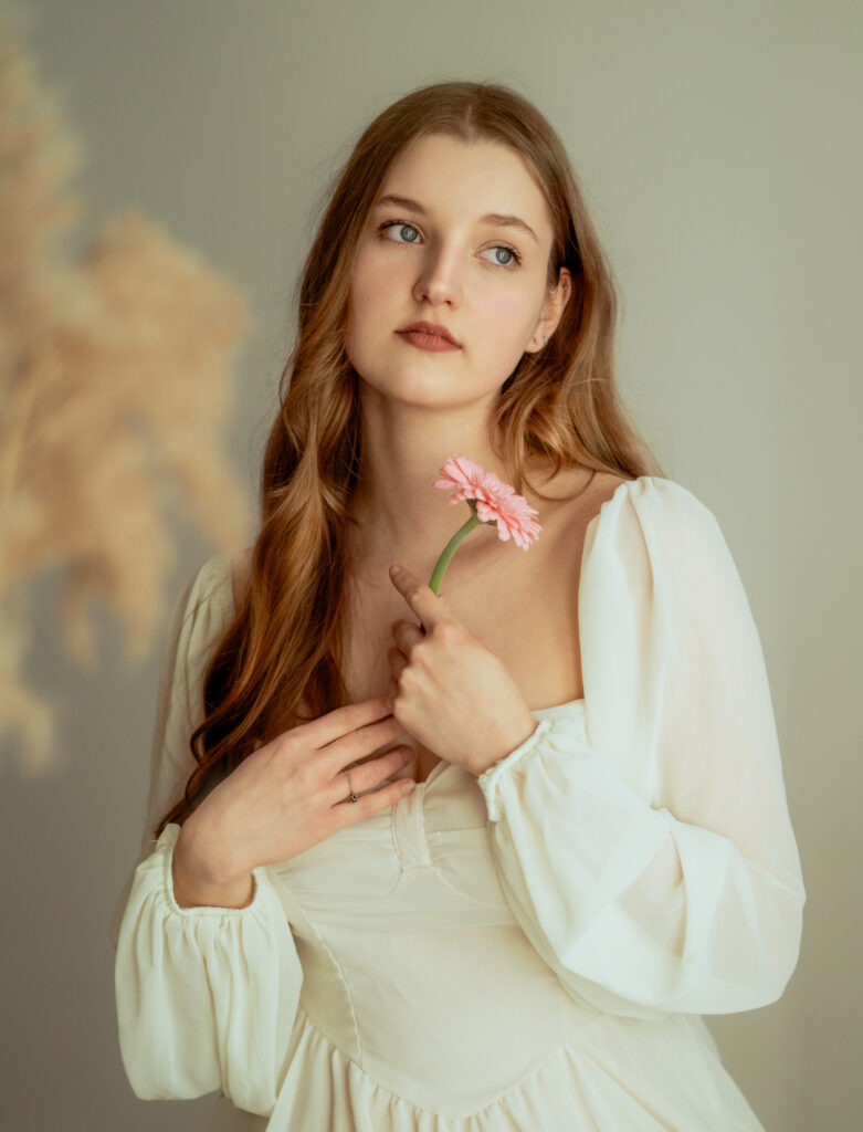 portret kobiety z kwiatami artystyczny portret kobiecy subtelna fotografia portretowa kobieta z delikatnymi kwiatami naturalne piękno romantyczny portret fotografia w ciepłym świetle kobieta trzymająca kwiaty miękkie światło ciepła kolorystyka minimalistyczne tło fotografia fine art portret studyjny pastelowe kwiaty estetyka naturalna